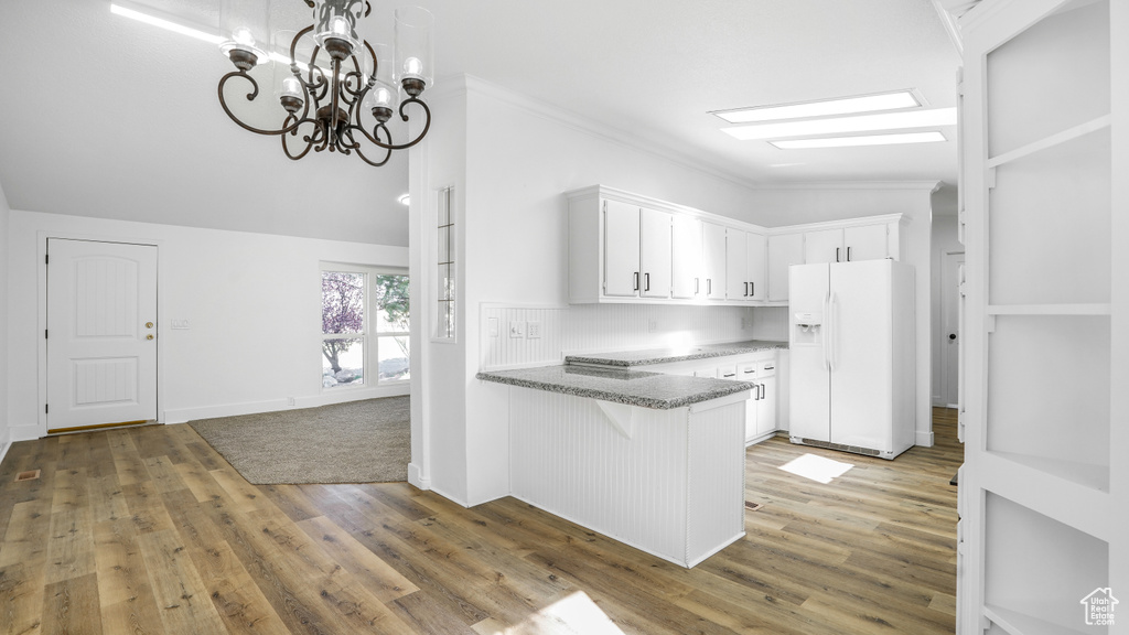 Kitchen featuring white cabinets, a peninsula, white fridge with ice dispenser, and light wood-type flooring