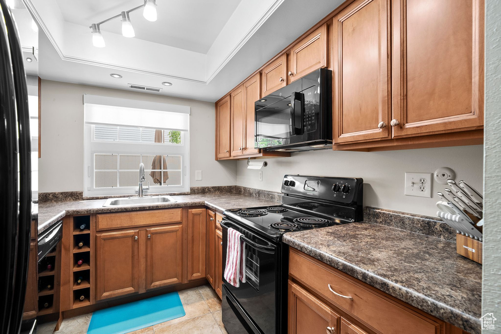 Kitchen featuring black appliances, brown cabinets, dark countertops, and a sink