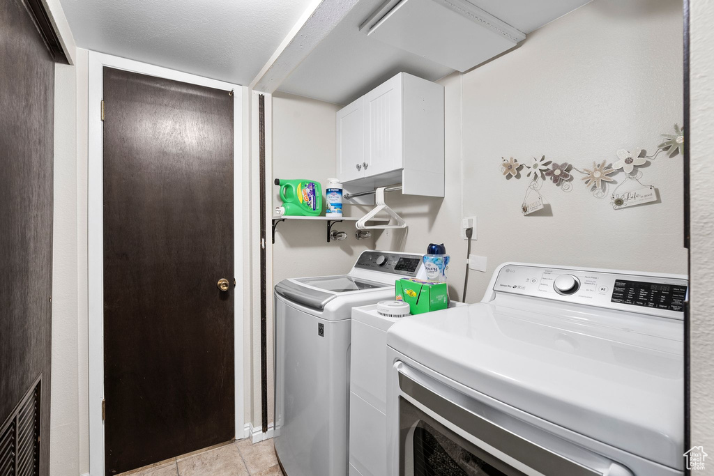 Washroom featuring washing machine and dryer, cabinet space, visible vents, and light tile patterned floors