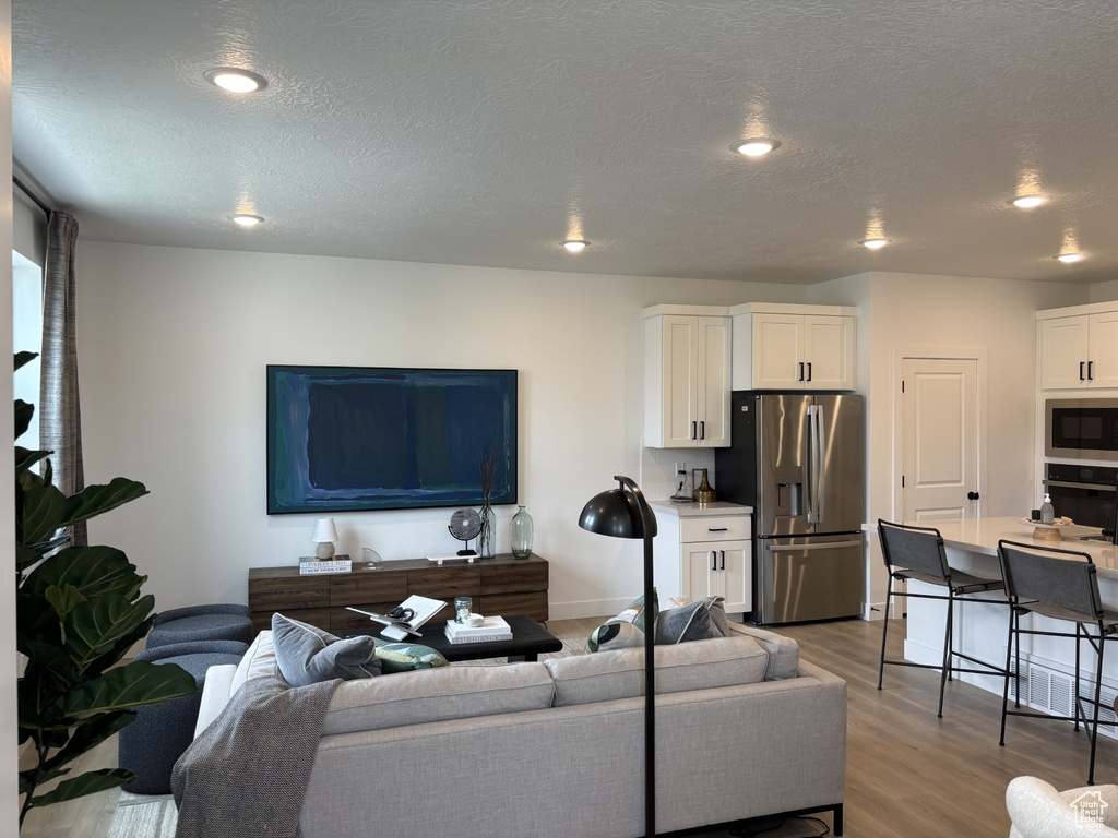 Living room with light wood finished floors, baseboards, a textured ceiling, and recessed lighting