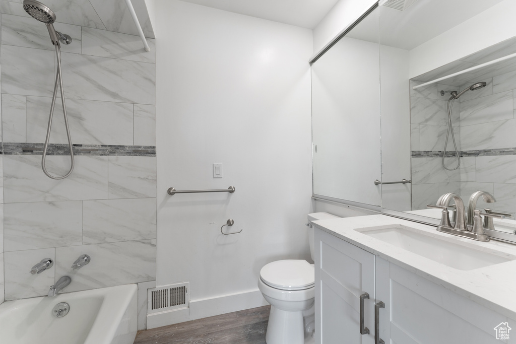 Bathroom with wood finished floors, vanity,  shower combination, toilet, and visible vents