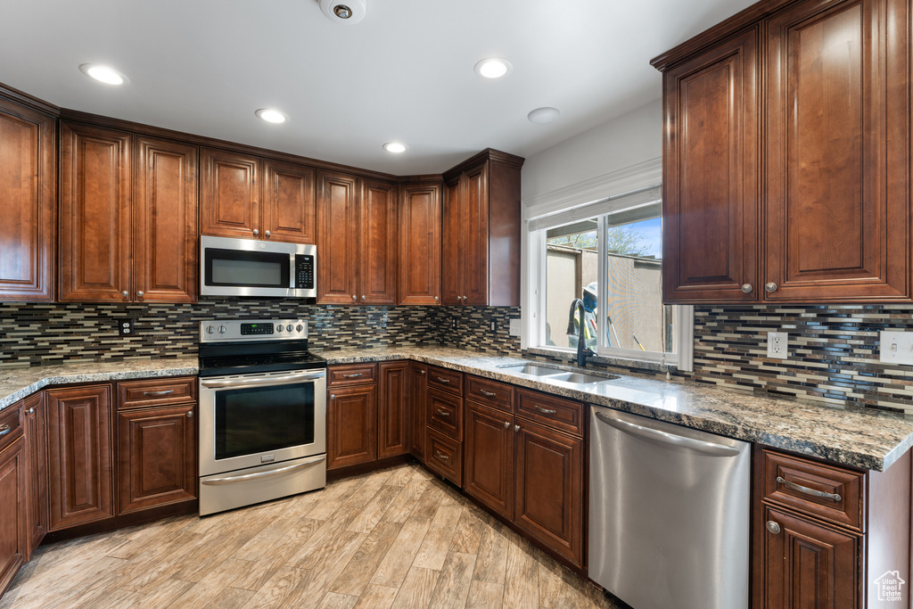 Kitchen with a sink, light wood-style floors, appliances with stainless steel finishes, and tasteful backsplash