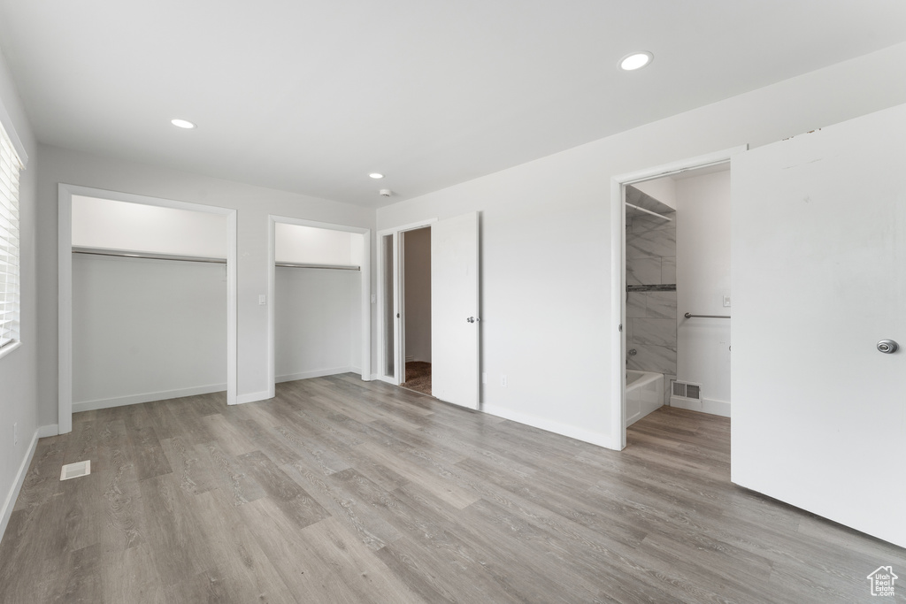 Unfurnished bedroom featuring light wood-style flooring, visible vents, recessed lighting, and two closets