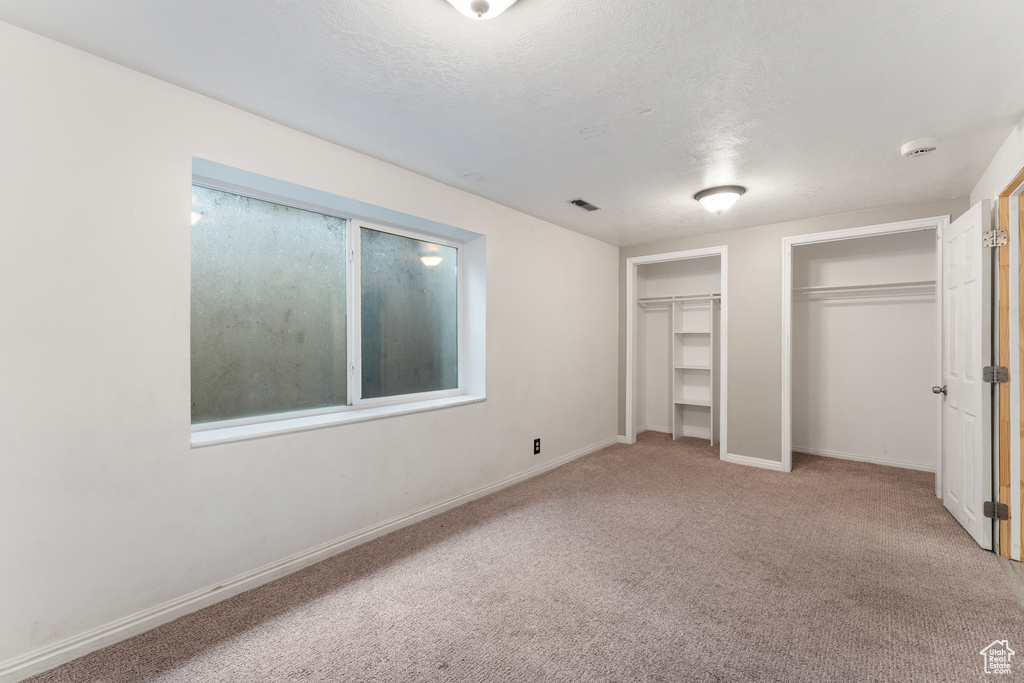Unfurnished bedroom featuring visible vents, baseboards, multiple closets, and carpet flooring