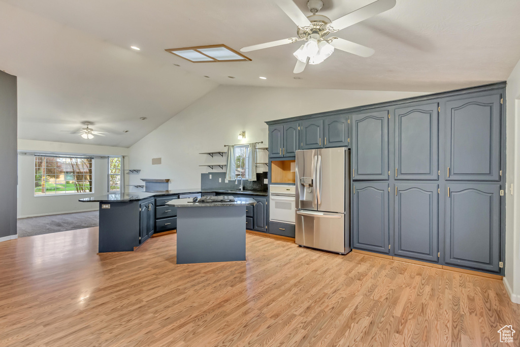 Kitchen with dark countertops, oven, ceiling fan, stainless steel fridge with ice dispenser, and a peninsula