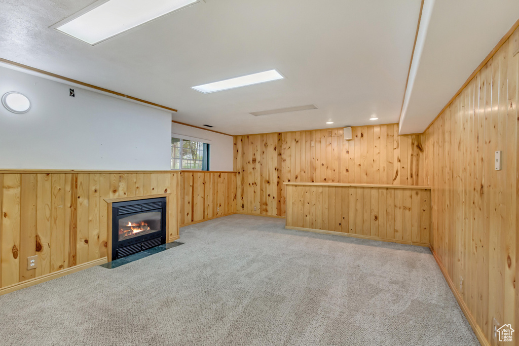 Unfurnished living room with a fireplace with flush hearth, wood walls, and carpet