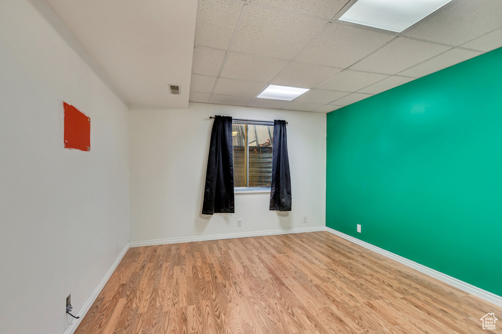 Unfurnished room with wood finished floors, visible vents, a drop ceiling, and baseboards