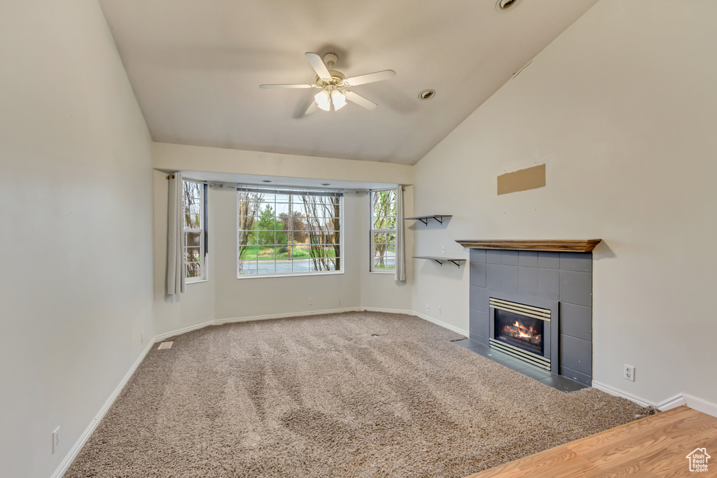 Unfurnished living room with lofted ceiling, a tiled fireplace, a ceiling fan, and baseboards