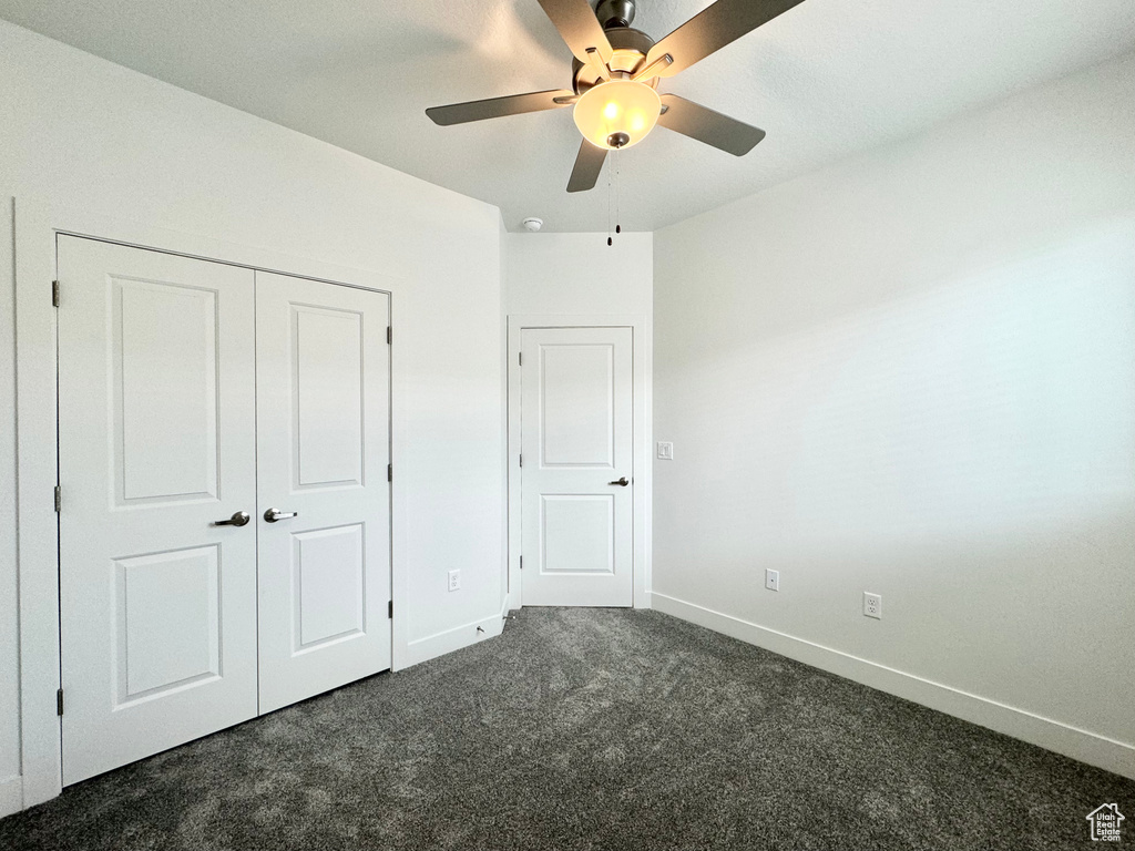 Unfurnished bedroom featuring baseboards, a ceiling fan, dark colored carpet, and a closet