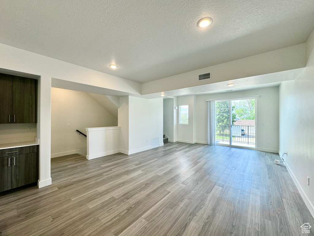 Unfurnished living room featuring a textured ceiling, light wood finished floors, baseboards, visible vents, and recessed lighting