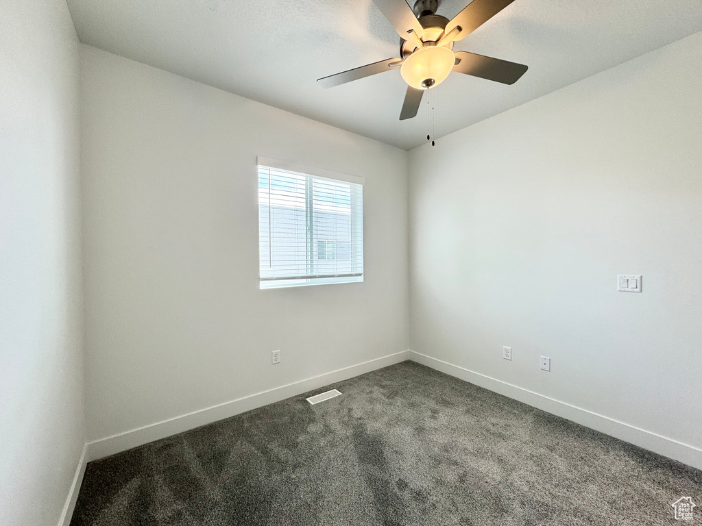 Unfurnished room with baseboards, dark colored carpet, visible vents, and ceiling fan