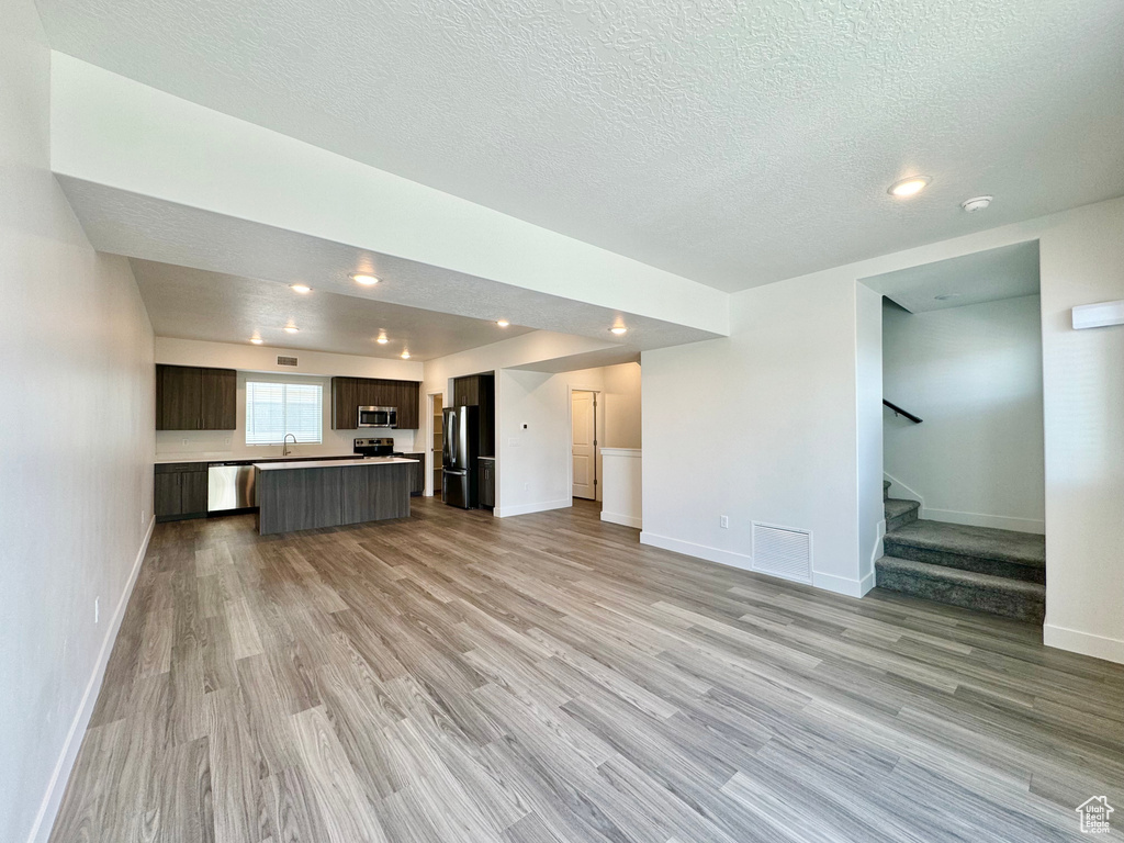 Unfurnished living room featuring a textured ceiling, stairs, light wood finished floors, baseboards, and visible vents