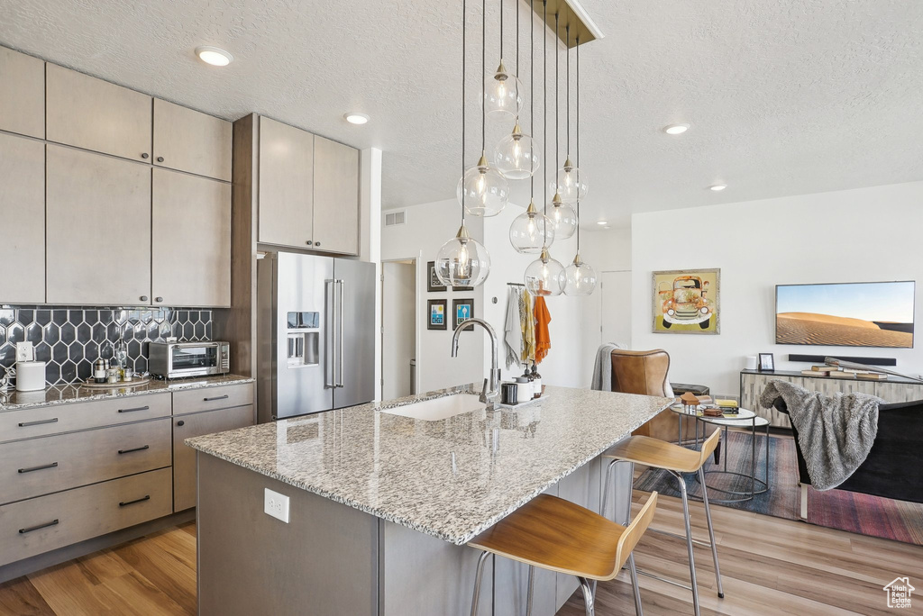 Kitchen with a breakfast bar area, a textured ceiling, a sink, light wood-style floors, and high end fridge