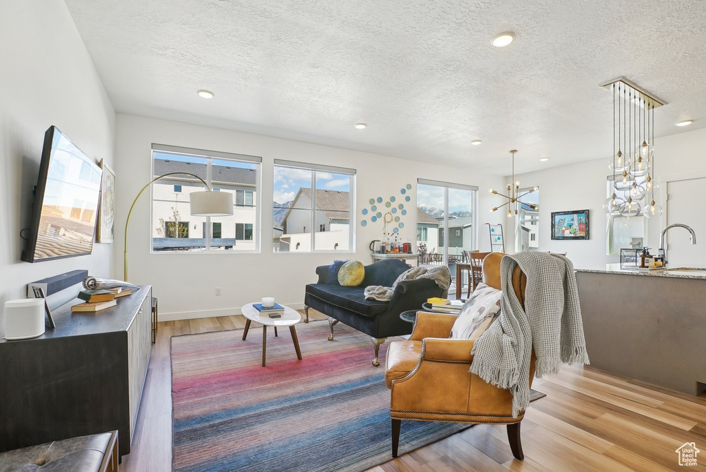 Living area with a textured ceiling, light wood-type flooring, baseboards, a notable chandelier, and recessed lighting
