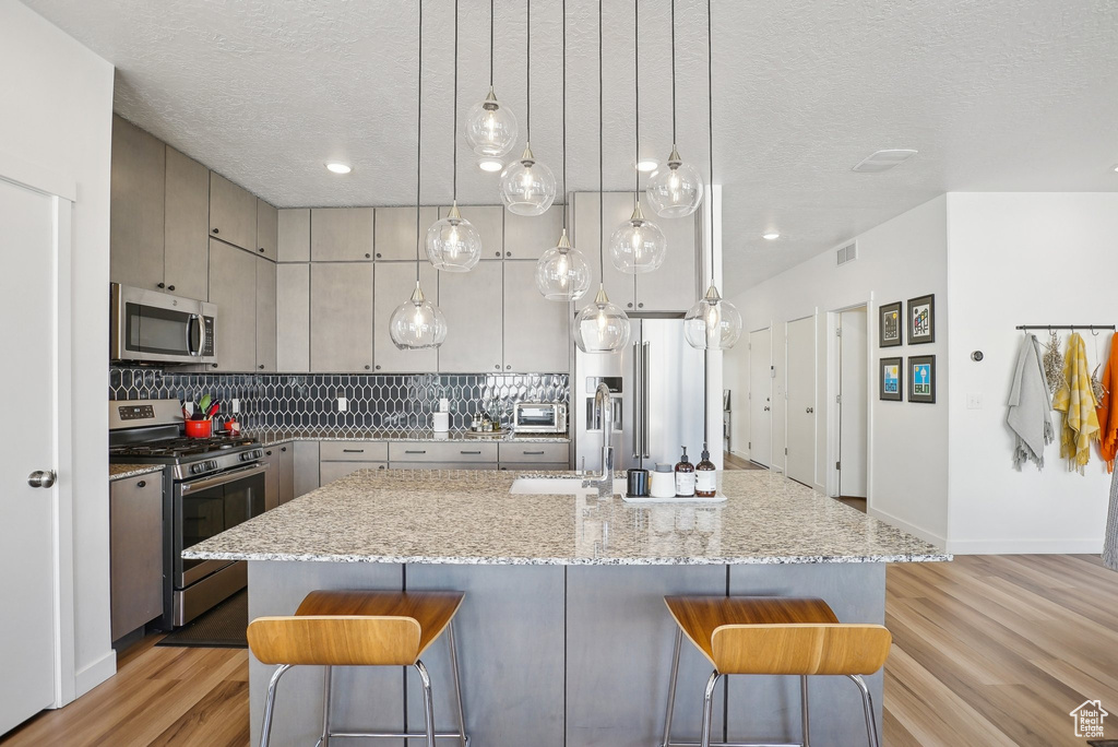 Kitchen with backsplash, stainless steel appliances, a breakfast bar area, and a textured ceiling
