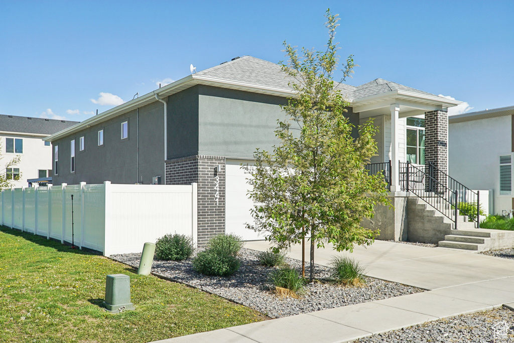 View of property exterior featuring fence, brick siding, concrete driveway, an attached garage, and a yard