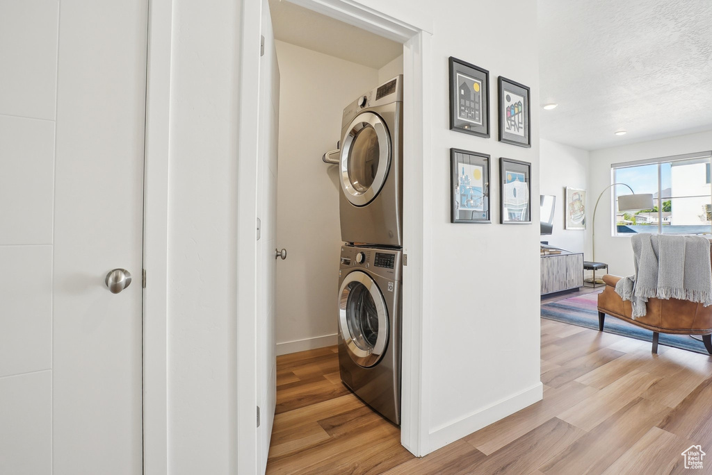 Washroom with stacked washer / drying machine, baseboards, laundry area, and light wood-style floors