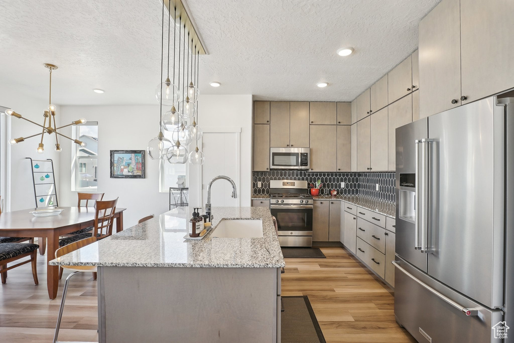 Kitchen with a notable chandelier, a sink, light wood-style floors, a textured ceiling, and stainless steel appliances