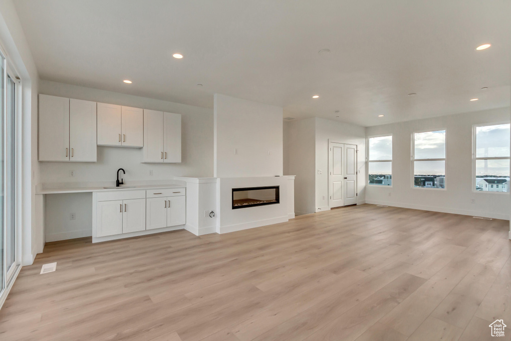 Unfurnished living room with recessed lighting, a sink, light wood-style floors, baseboards, and a glass covered fireplace