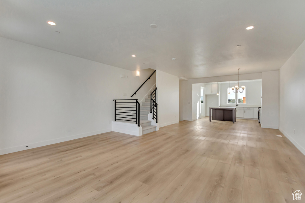 Unfurnished living room featuring light wood-style flooring, baseboards, a chandelier, and stairway