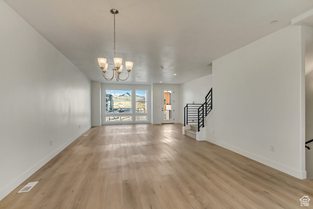 Unfurnished living room featuring stairway, baseboards, light wood-style flooring, and an inviting chandelier