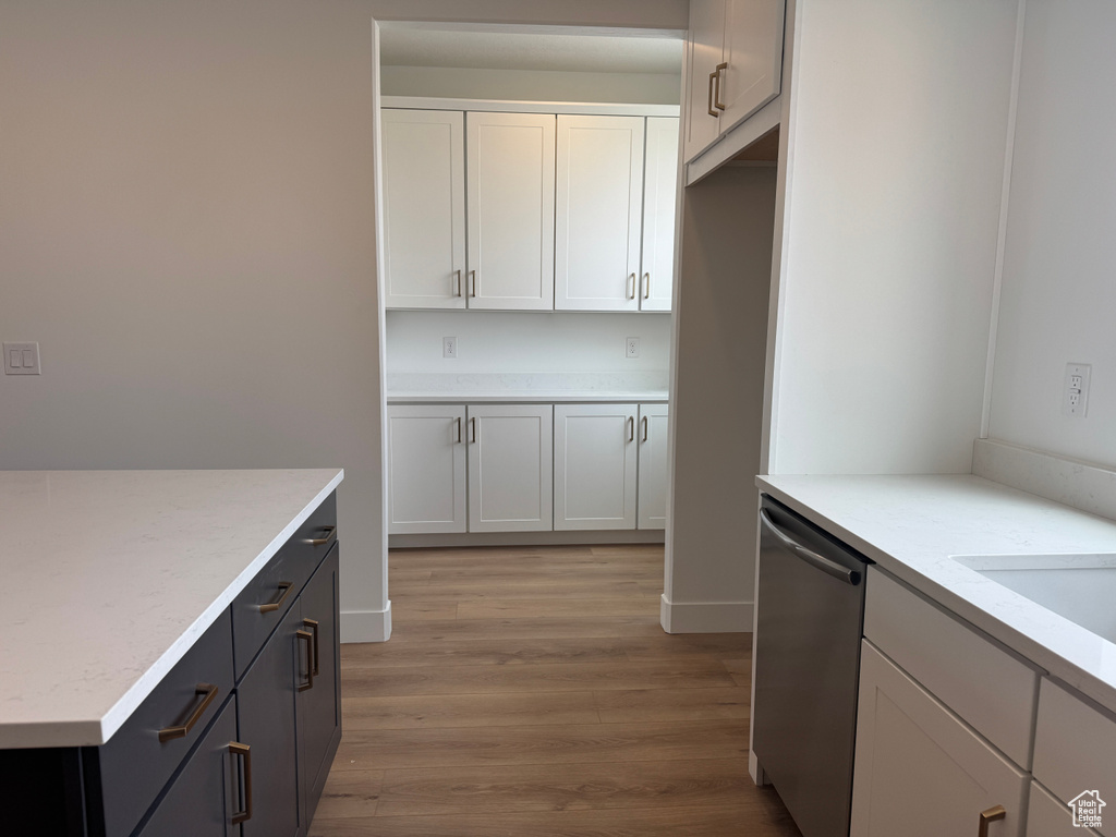 Kitchen featuring white cabinets, stainless steel dishwasher, light stone counters, and light wood-style flooring