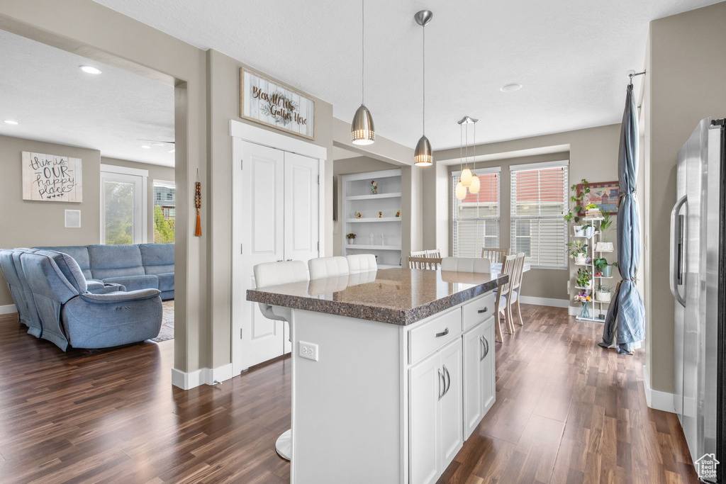 Kitchen featuring freestanding refrigerator, a breakfast bar, baseboards, and dark wood-style flooring