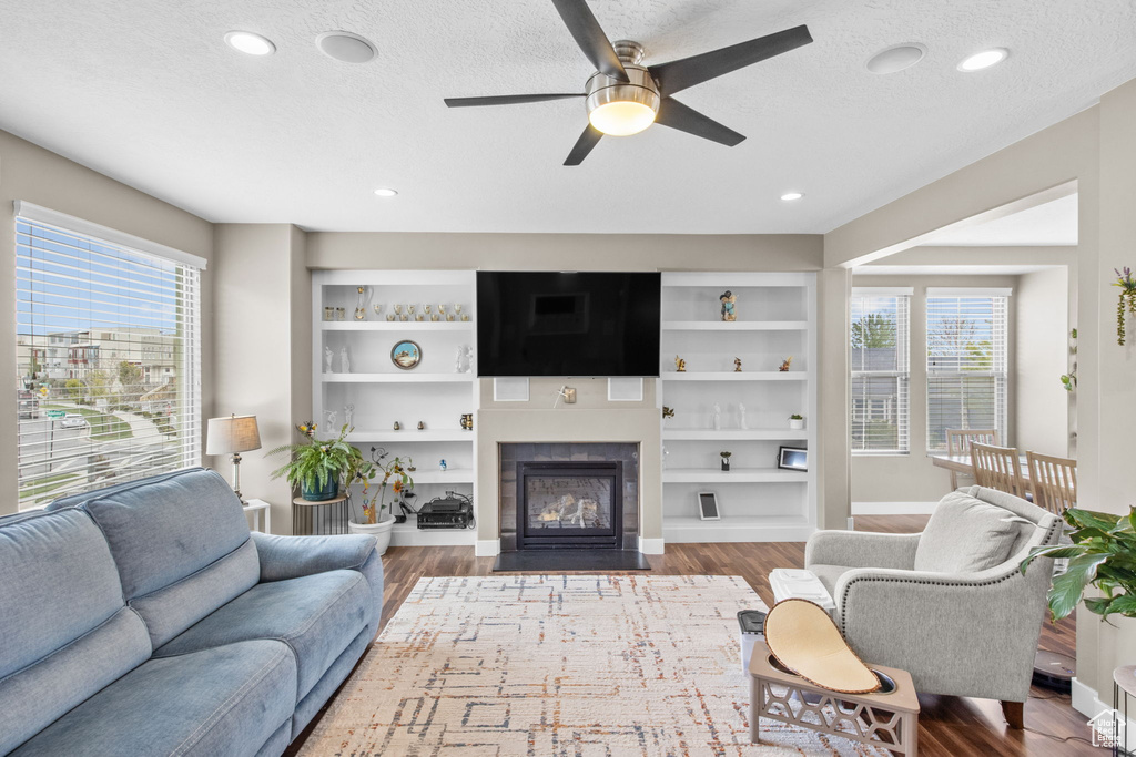 Living room featuring a fireplace with flush hearth, wood finished floors, a textured ceiling, and ceiling fan