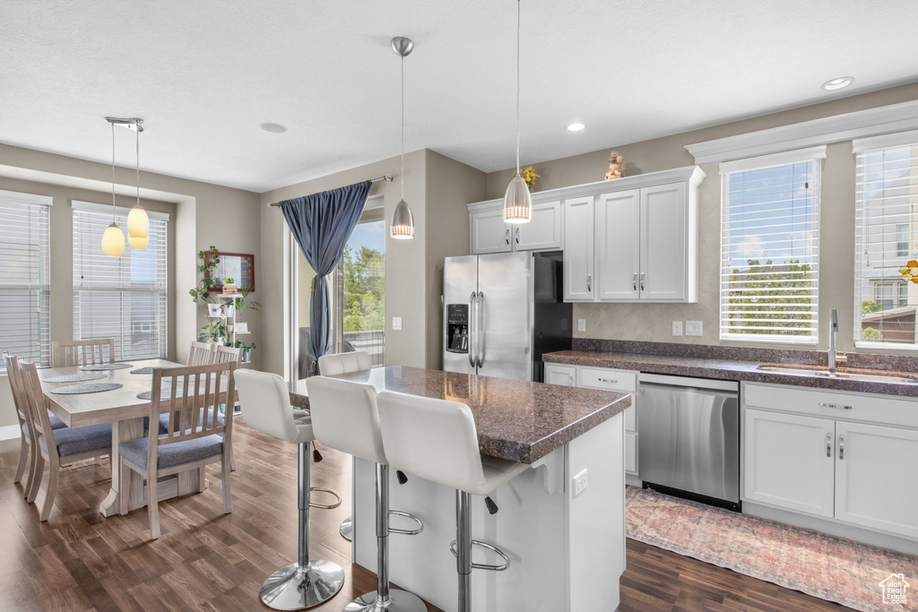 Kitchen featuring white cabinets, a sink, a center island, appliances with stainless steel finishes, and dark wood-style flooring