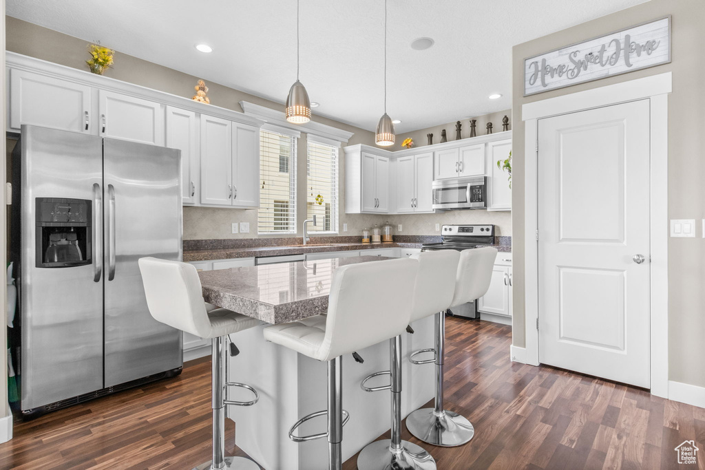 Kitchen with white cabinets, a breakfast bar, stainless steel appliances, decorative light fixtures, and dark wood finished floors