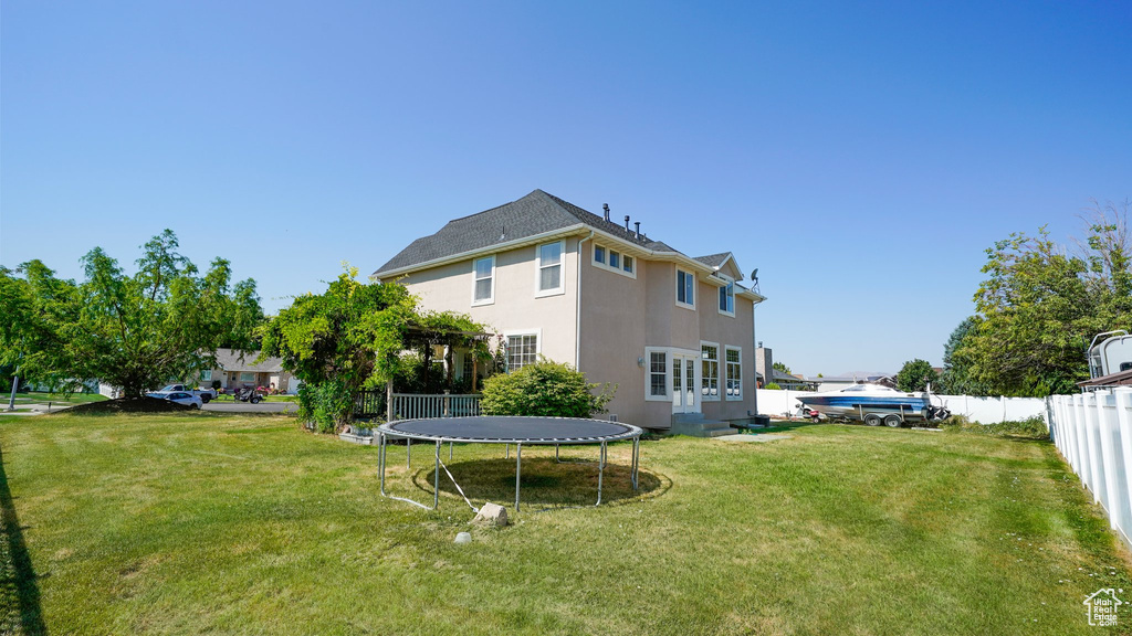 Rear view of house with fence, a lawn, stucco siding, and a trampoline