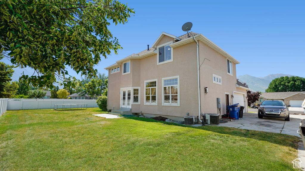 Rear view of property with stucco siding, central air condition unit, a lawn, and fence