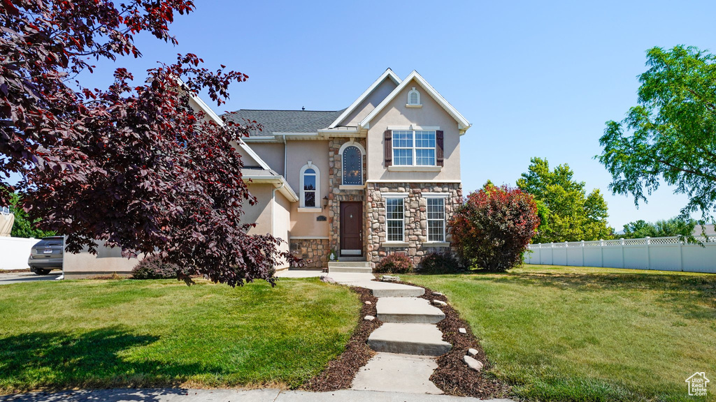 Traditional home featuring stone siding, a front yard, stucco siding, and fence