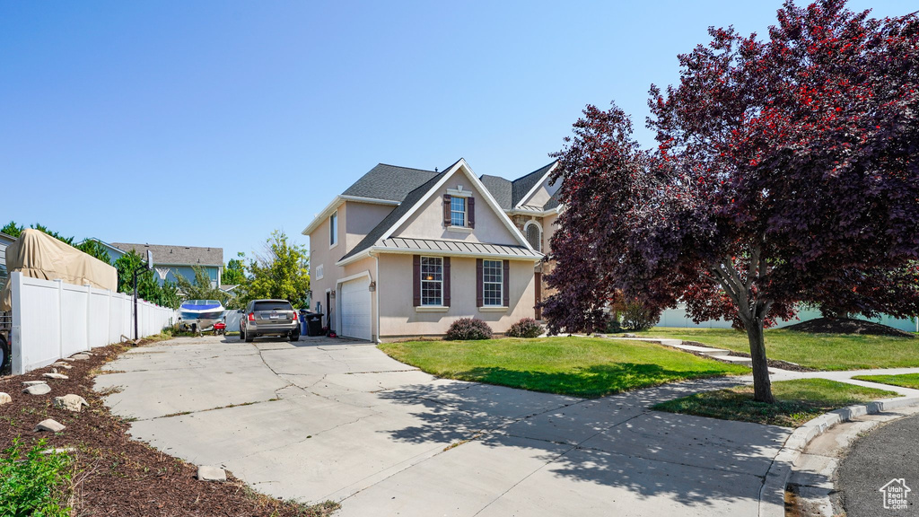 Traditional-style house featuring stucco siding, a front lawn, driveway, and fence