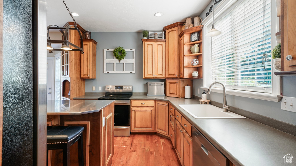 Kitchen featuring stainless steel appliances, open shelves, a sink, light wood-type flooring, and a breakfast bar area
