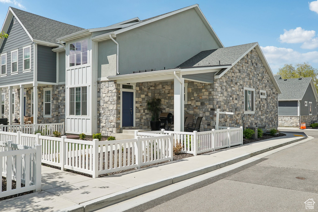 View of front of home featuring board and batten siding, stone siding, a shingled roof, stucco siding, and a fenced front yard