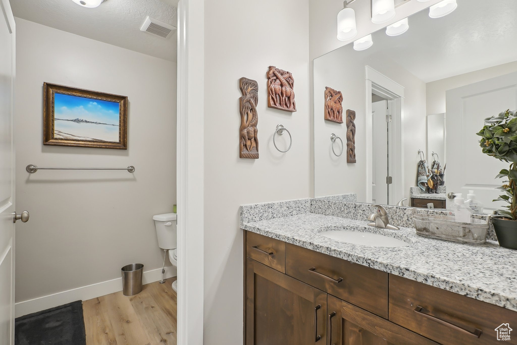 Bathroom with wood finished floors, toilet, vanity, baseboards, and visible vents
