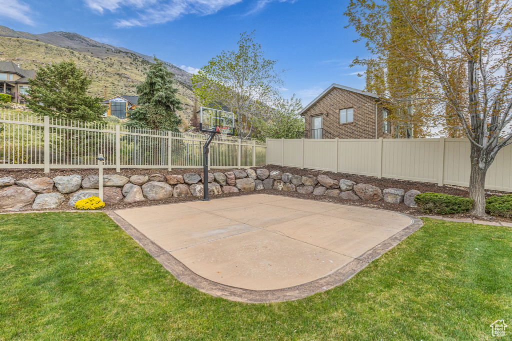 View of basketball court featuring a fenced backyard, a lawn, basketball court, and a mountain view