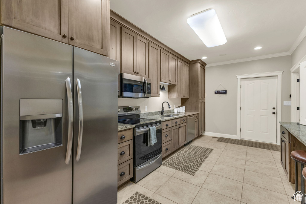 Kitchen featuring a sink, light tile patterned flooring, light stone countertops, crown molding, and appliances with stainless steel finishes
