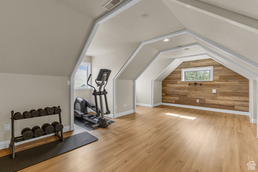 Bonus room with baseboards, visible vents, lofted ceiling, wood finished floors, and wooden walls