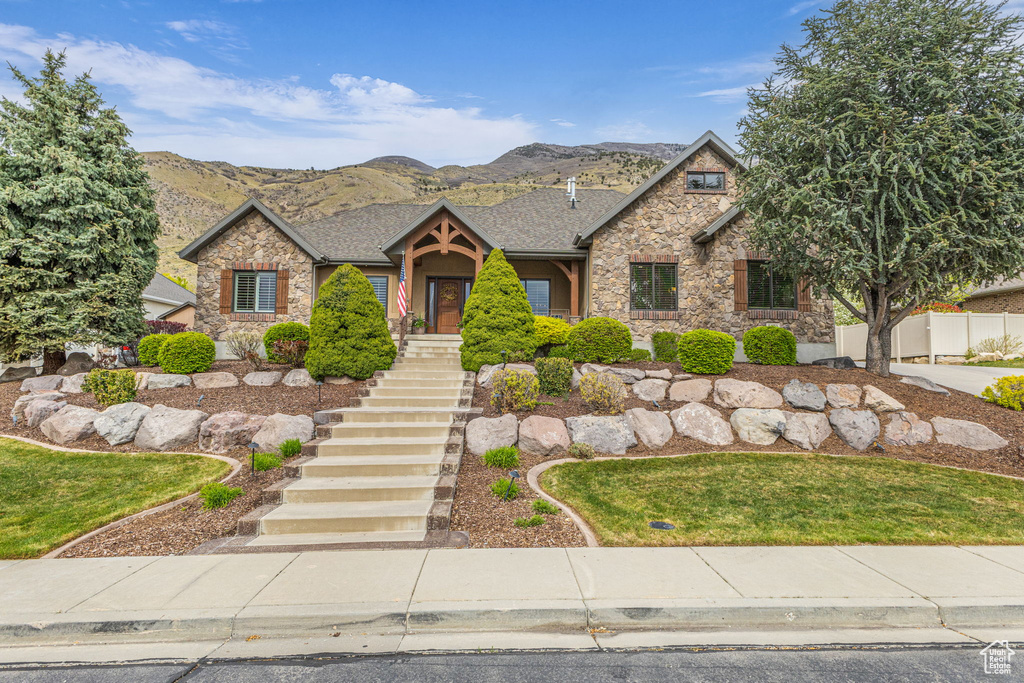 View of front of house with stone siding, a mountain view, fence, roof with shingles, and stairs