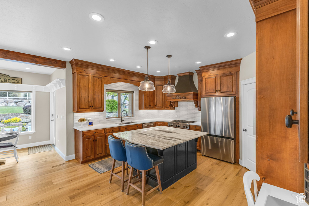 Kitchen featuring stainless steel appliances, a sink, brown cabinetry, and custom range hood