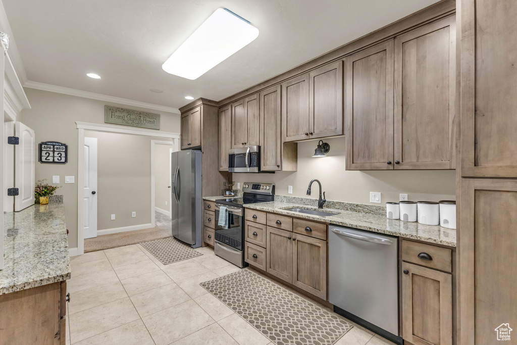 Kitchen with stainless steel appliances, a sink, ornamental molding, light stone counters, and light tile patterned floors