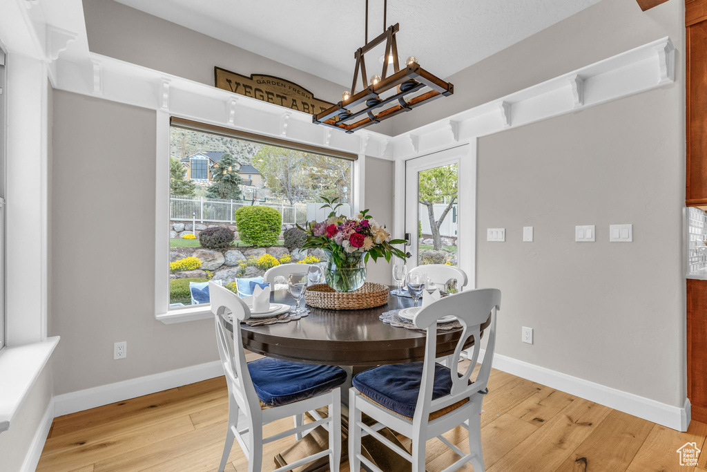 Dining area with baseboards, a wealth of natural light, light wood-style floors, and an inviting chandelier