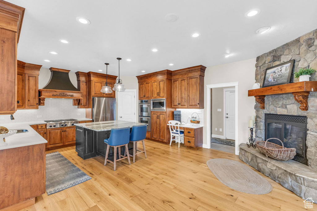 Kitchen featuring a kitchen bar, stainless steel appliances, premium range hood, backsplash, and a kitchen island