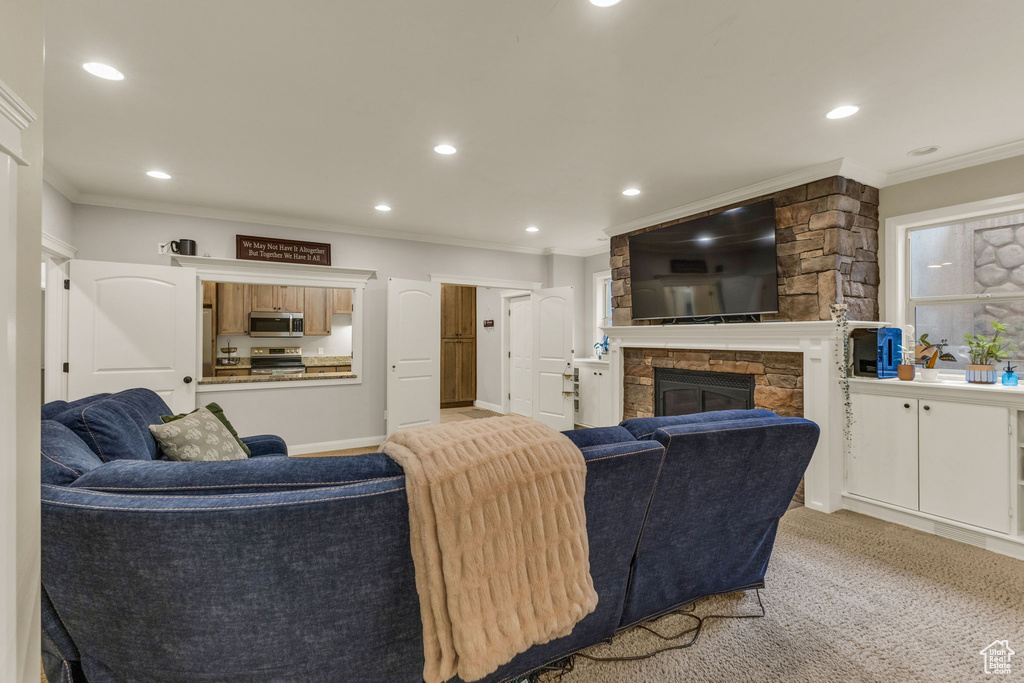 Living room with a stone fireplace, recessed lighting, ornamental molding, and light colored carpet