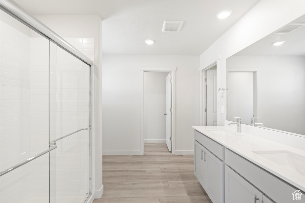 Full bath with wood finished floors, a shower stall, double vanity, and recessed lighting