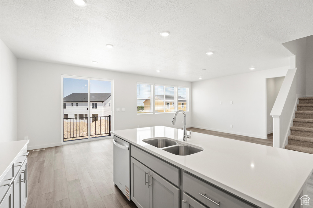 Kitchen with dishwasher, light countertops, a center island with sink, gray cabinets, and light wood-style flooring