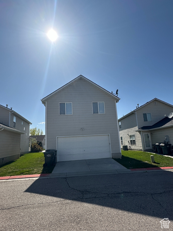View of front of home featuring concrete driveway, a front yard, cooling unit, and a garage