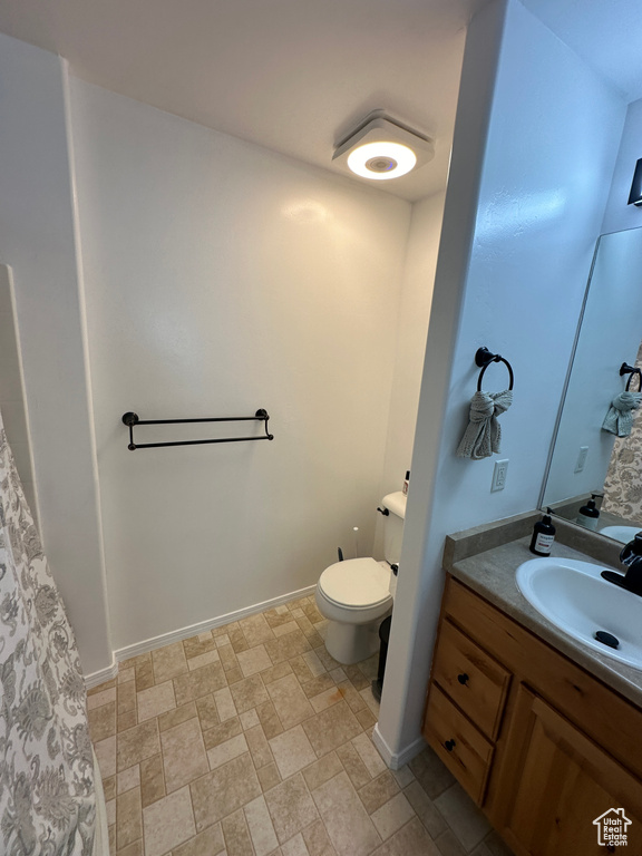 Bathroom with toilet, stone finish floor, vanity, and baseboards